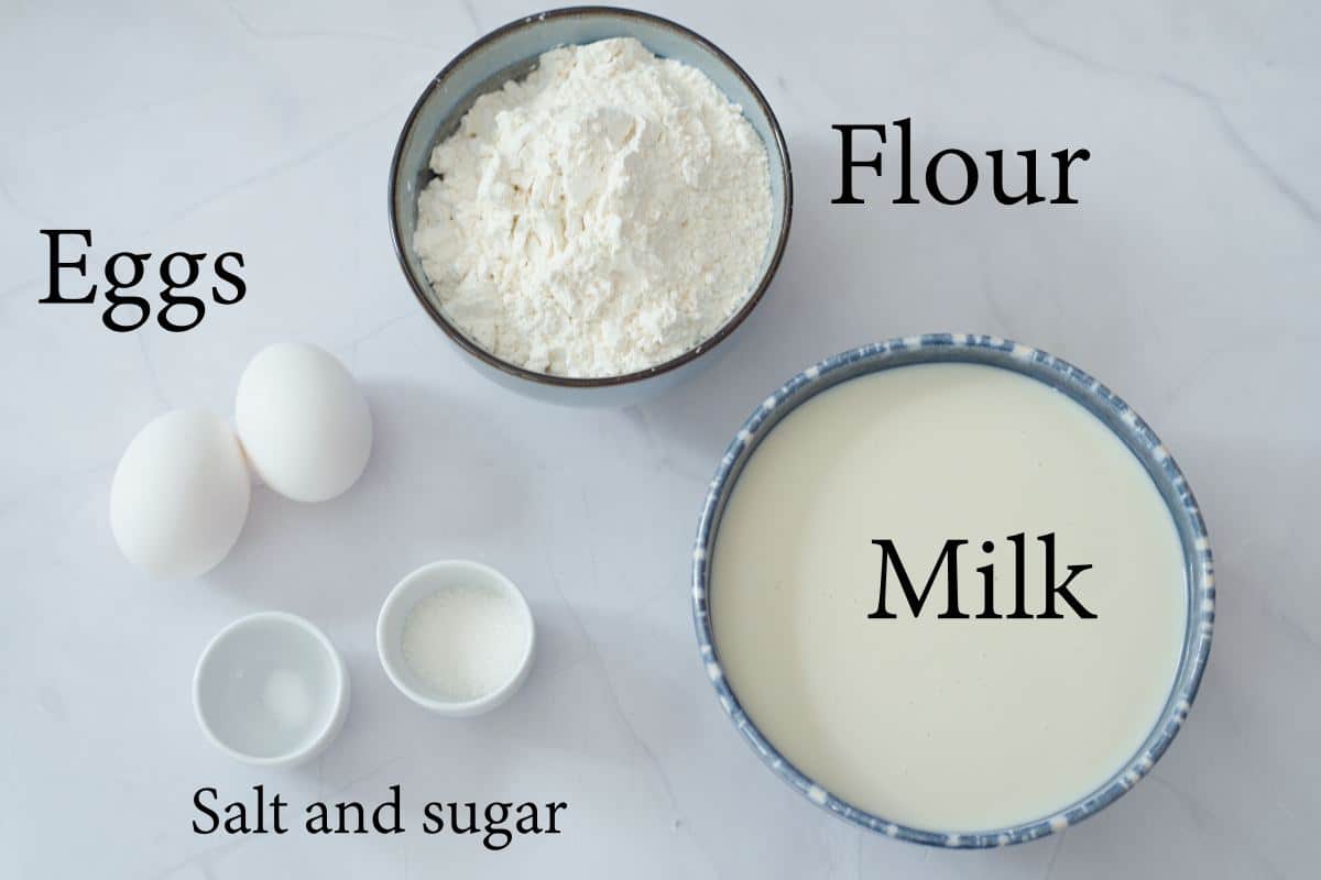milk, flour, eggs, salt and sugar on white countertop in bowls. 