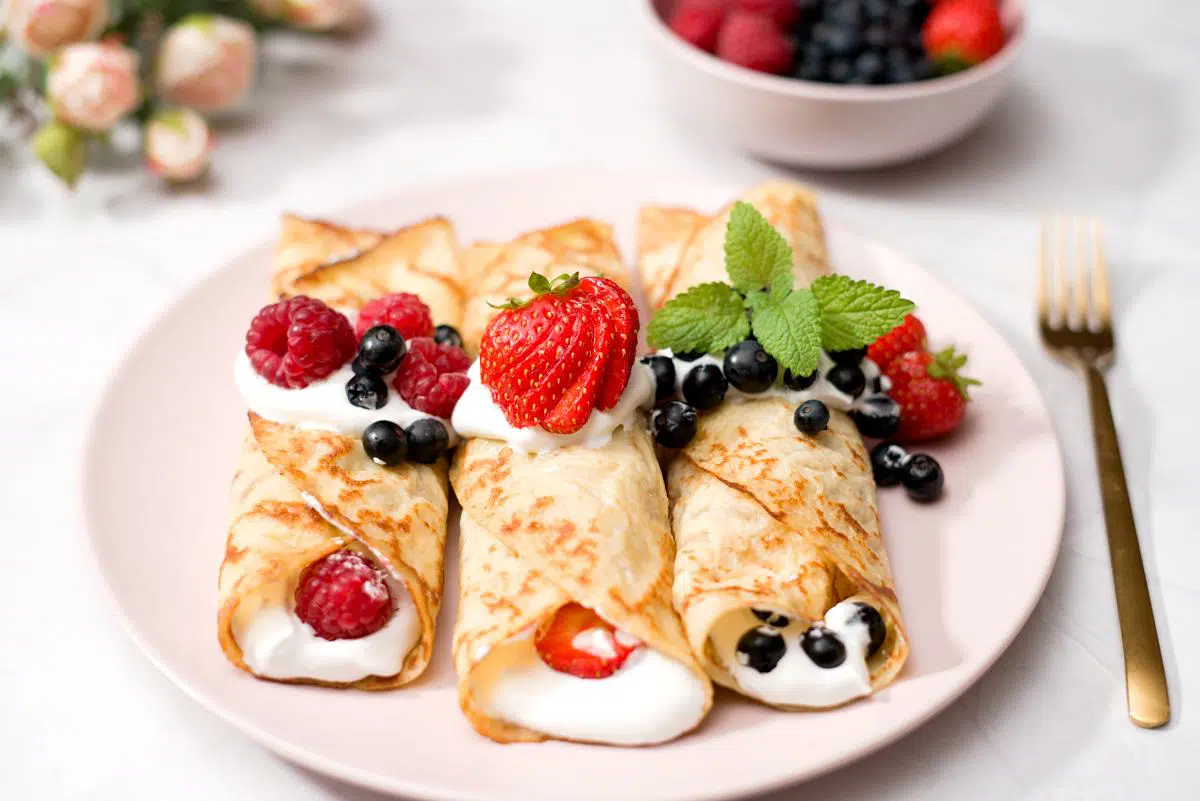Three rolled pancakes with creme and berry filling decorated with fresh berries. 