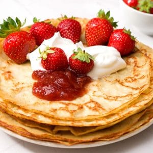 flat pancakes on a pile with jam and strawberries.
