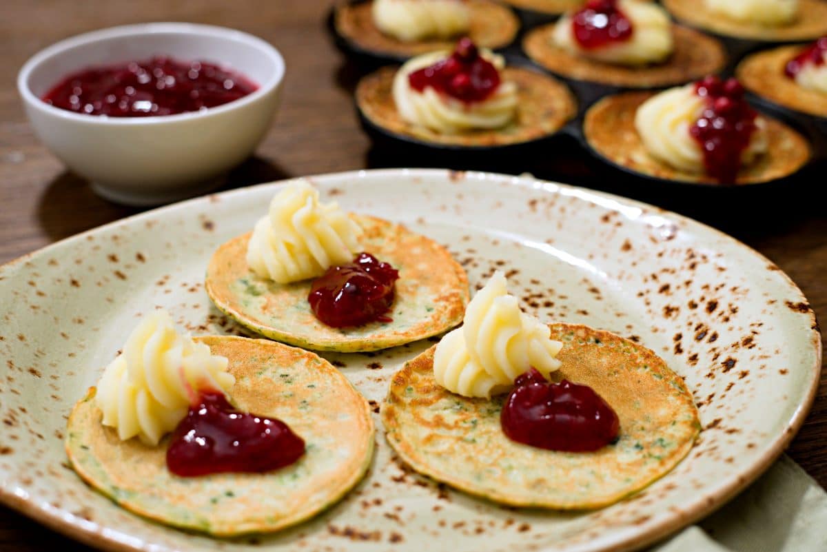 Three small spinach pancakes on plate with mashed potatoes and lingonbeery jam. 