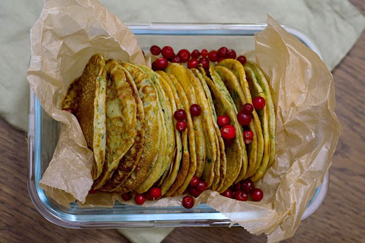 a stack of thin green pancakes in glassware container wrapped in baking paper. 