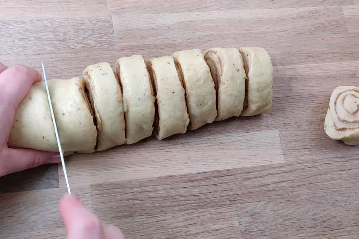 hands with knife cutting bun dough roll into slices. 