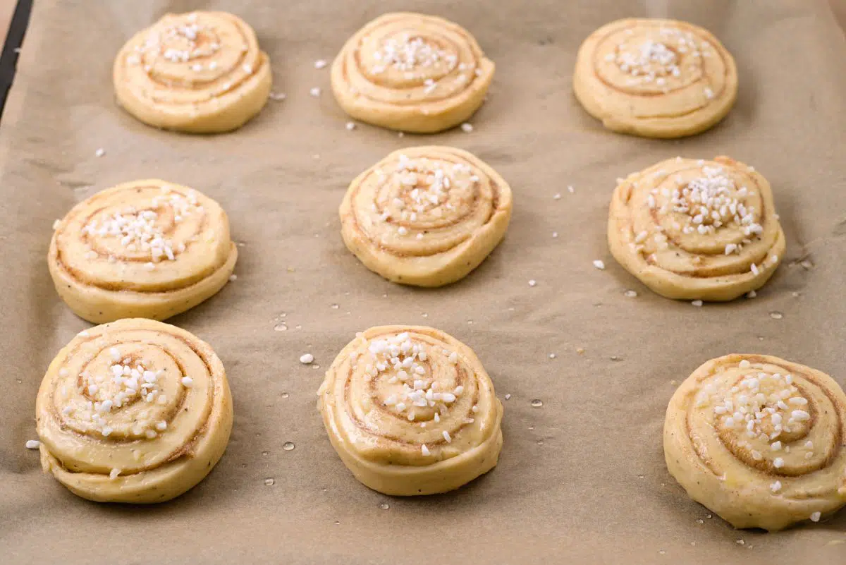 nine cinnamon rolls on baking tray with pearls sugar on top of them. 