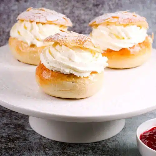 three cream filled buns on plate with a jam cum next to them.