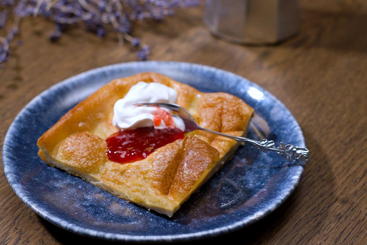 Pancake slice on blue plate with strawberry jam and whipped cream with little fork. 