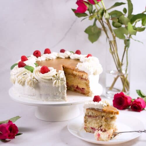 big cake with whipped cream, raspberries, caramel topping on a cakestand with roses.