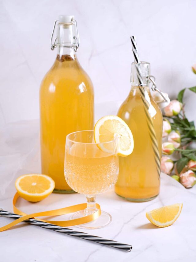 Yellow drink in glass and bottles with some fizzy bubbles. 