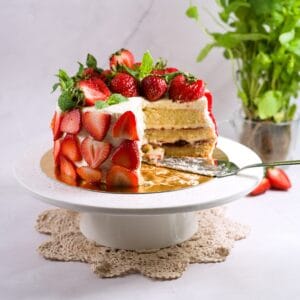 strawberry layer cake on wjhite cake stand with cut up piece.