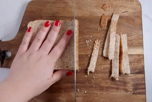 whole grain bread, cutting edges away on a board.