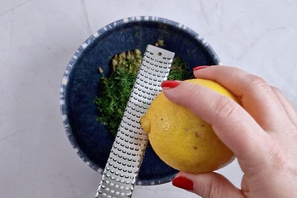 grating lemon with a microplane to a bowl.