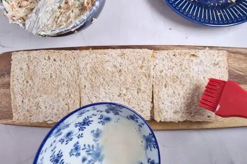 three white bread slices on board moistened with milk with a silicone brush. 