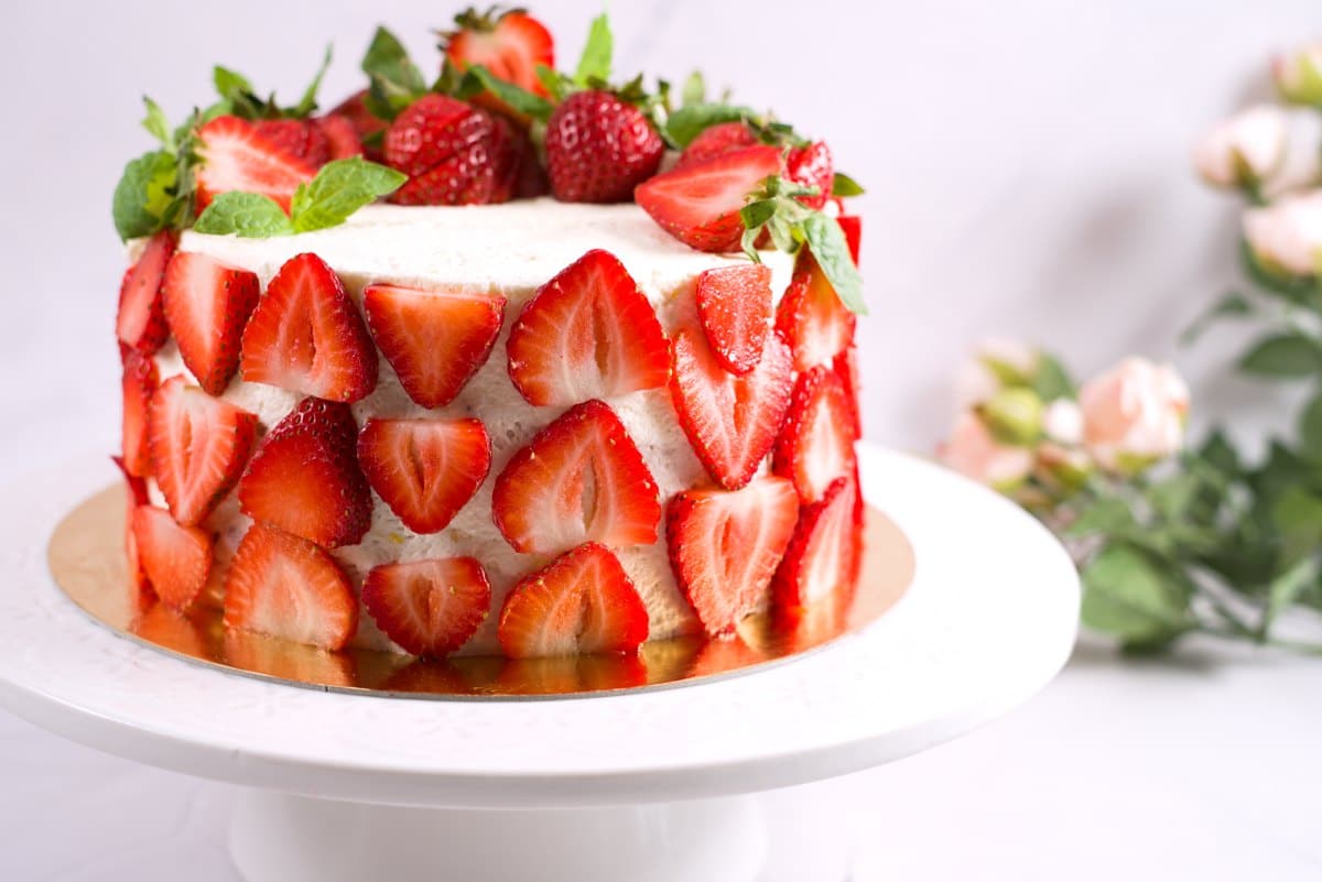 layer cake with whipped cream and strawberry slices on the sides and whole ones on top on one side. 