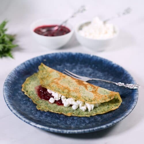 folded nettle pancake on blue platter with lingonberry jam.