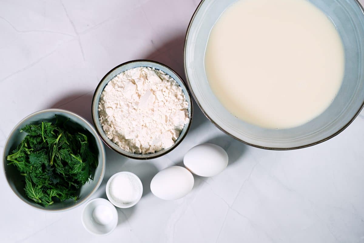 milk, flour, nettles in bowls and eggs on table. 