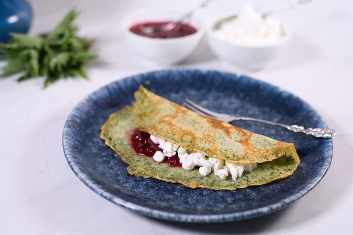 nettle pancake with cottage cheese filling on blue plate and jam jar in background.