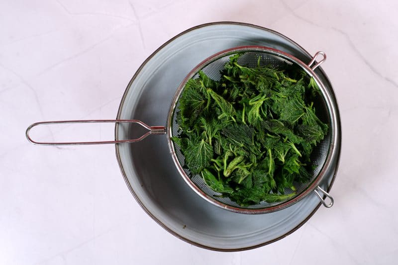 blanched nettles in sieve that is on top of a bowl.
