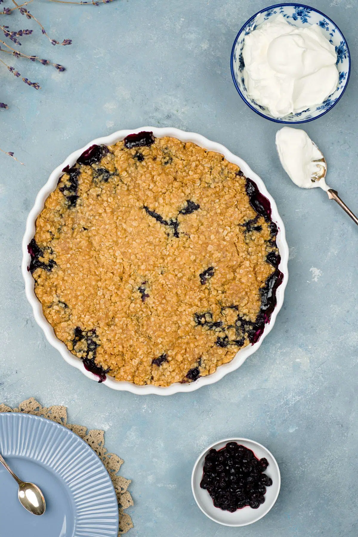 Blueberry crumble pie in white pan and whipped cream bowl.