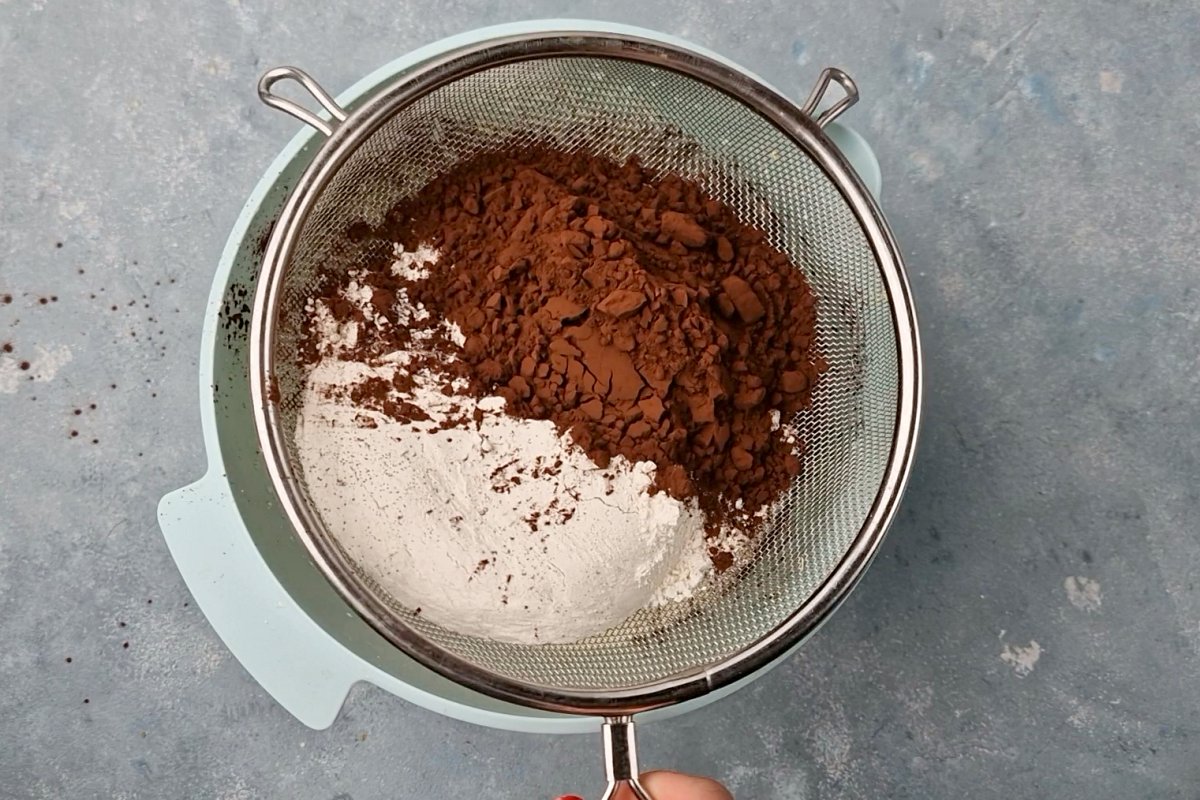 cocoa and flour in sieve on top of plastic bucket. 