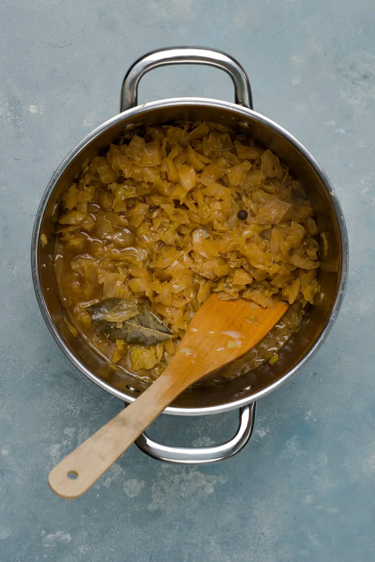 brown cabbage stew in silver big pot with wooden spoon. 