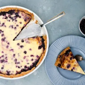 Blueberry pie in a white pan and a slice on blue plate.