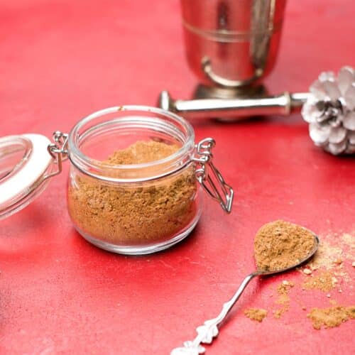 brown spice blend in small jar and red background.