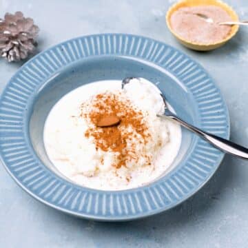 white rice porridge served with an almond on top. one plate on blue background.