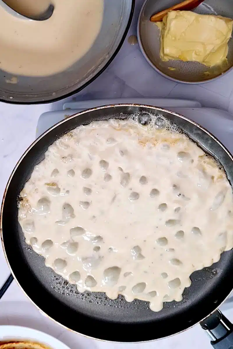 Pancake batter bubbles on pan, pan is turned to swirl the batter around. 