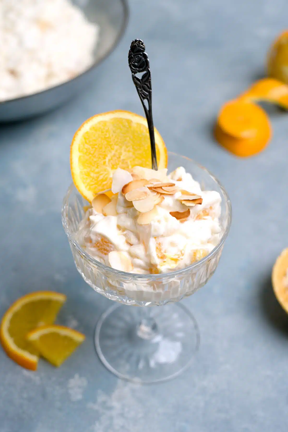 Rice dessert with some orange pieces in a shanpagen glass decorated with toasted almond slices and a slice of orange. 