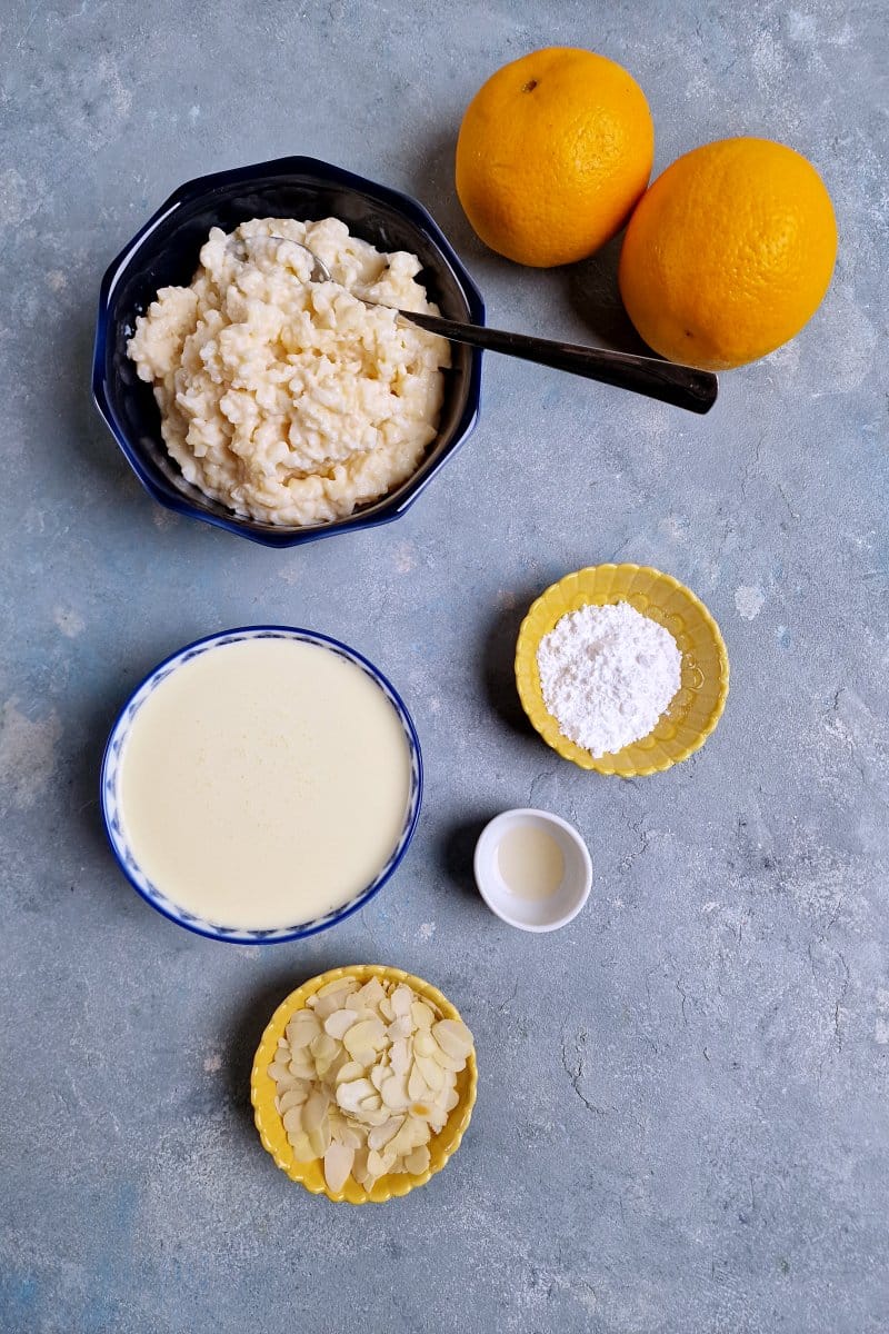 Ingredients in blue bowls, rice porridge, cream, oranges, sugar, almonds and vanilla. 