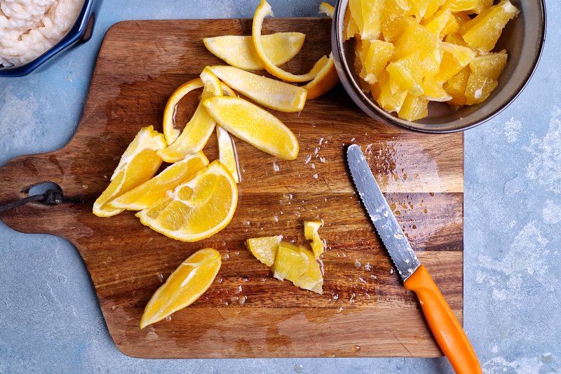 chopped orange pieces and peels on cutting board and in a bowl with orange knife. 