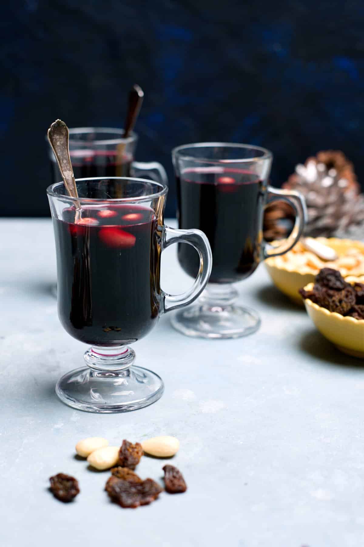 small glasses with mulled wine and yellow bowls with raisins and almonds, set decorated with pines. 