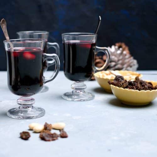 three small glögg glasses with red drink and almonds and raisins.