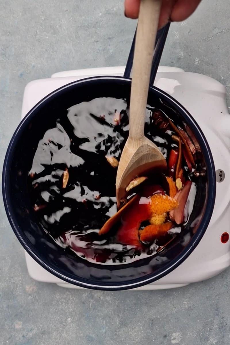 mixing mulled wine on heat with wooden spoon. 