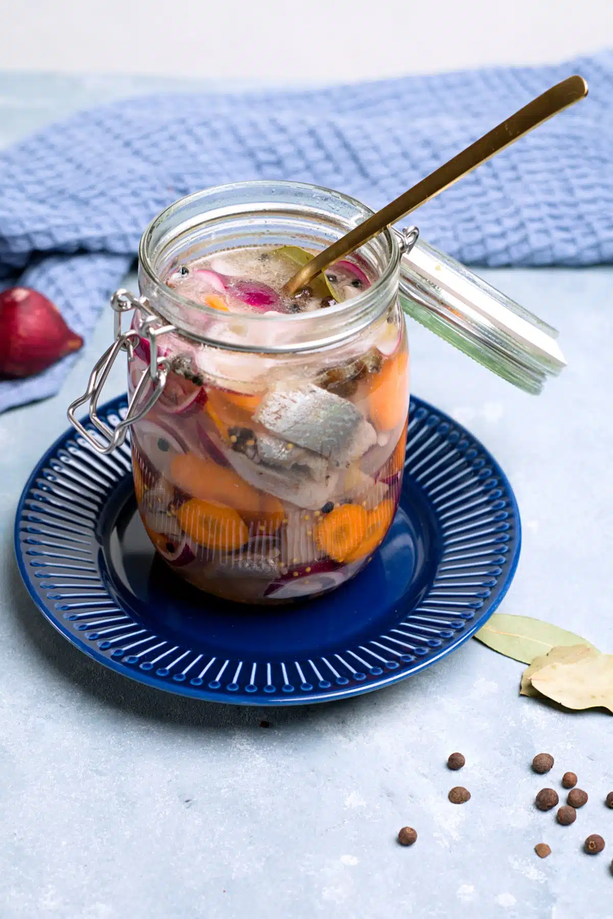 glass jar with fish pieces, carrot slices, red onion and pickle. 