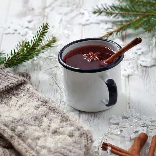 a white enamel mug with red glögg and cinnamon stick. 