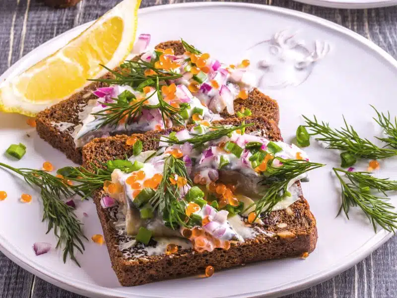 open faced rye sandwich with pickled herring, sill, lemon wedge and roe. 