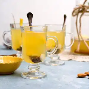 three glasses with yellow drink, raisins and almonds.