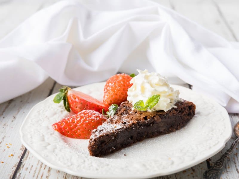 chocolate cake piece with whipped cream and slices fresh strawberries on white plate. 