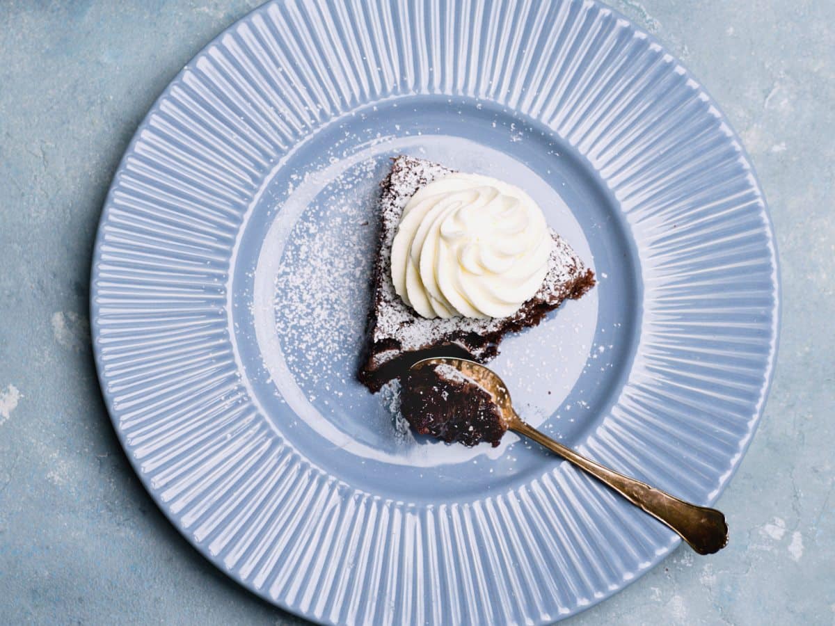 one large piece of chocolate cake with powdered sugar and cream on plate woth a little antique silver spoon. 
