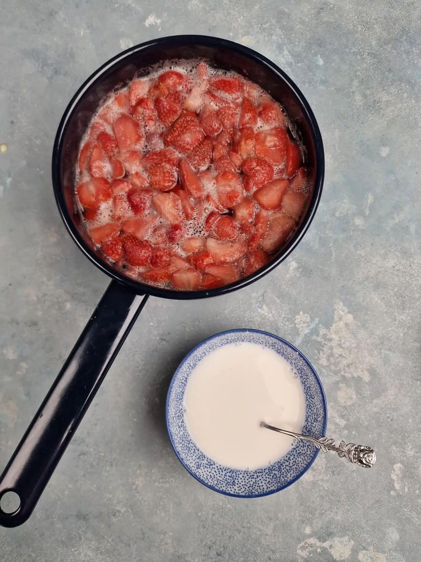 a white slurry mix in small bowl next to strawberry soup pan. 