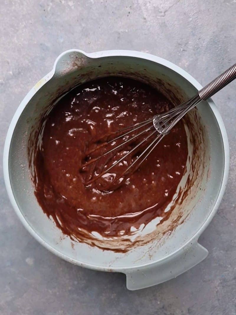 brown batter in bowl with a hand whisk. 