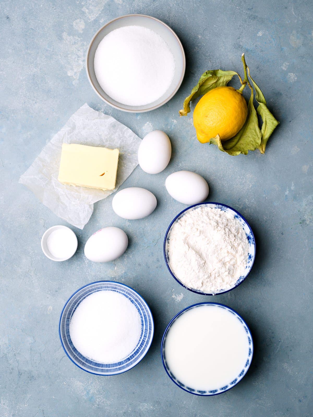 eggs, flour, sugar, butter, milk in bowls and a fresh lemon. 
