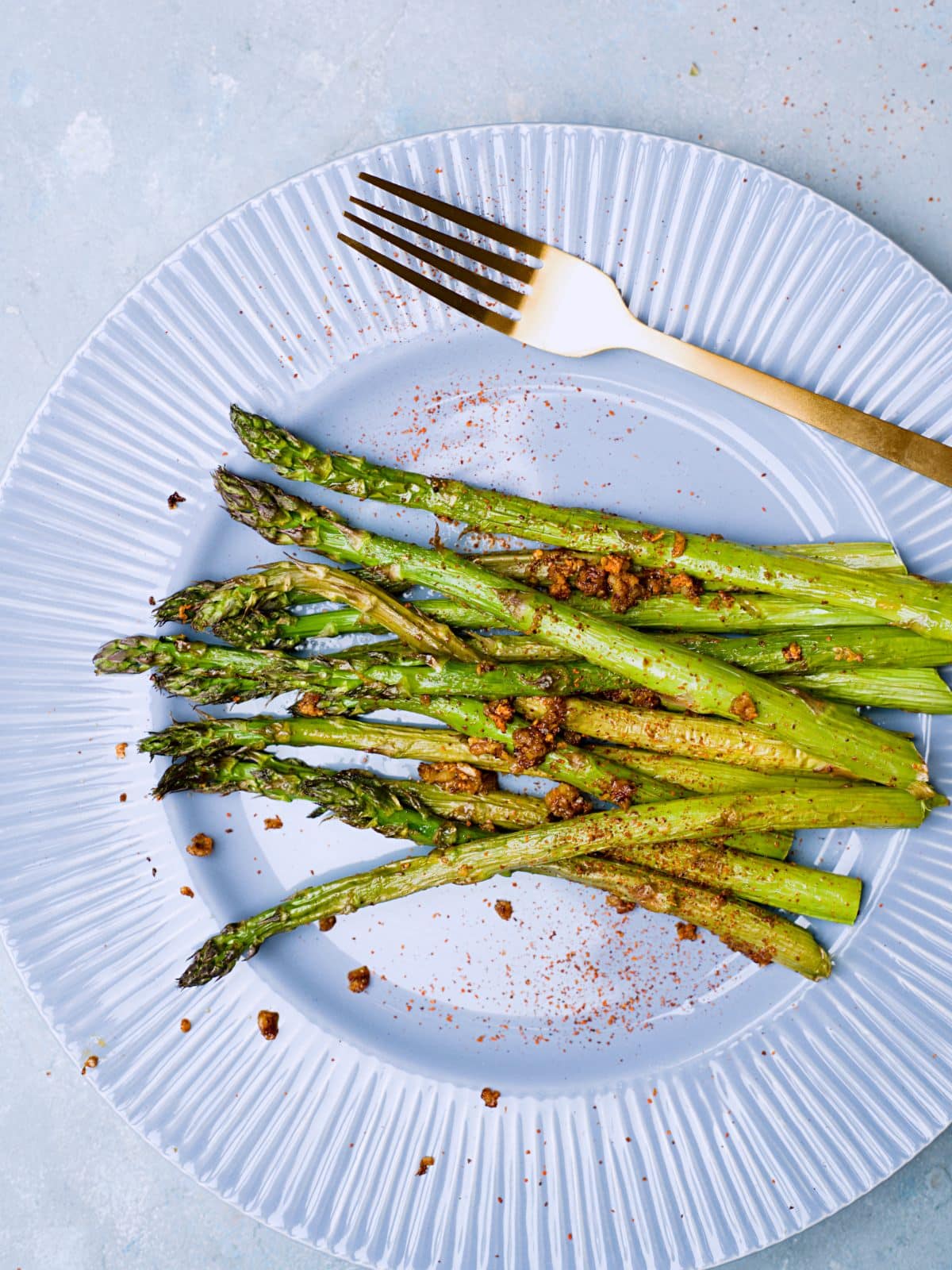 Green asparagus with garlic and chili on blue plate with golden fork. 
