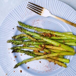 Green asparagus stalks on blue plate with golden fork and some garlic and chili on top.