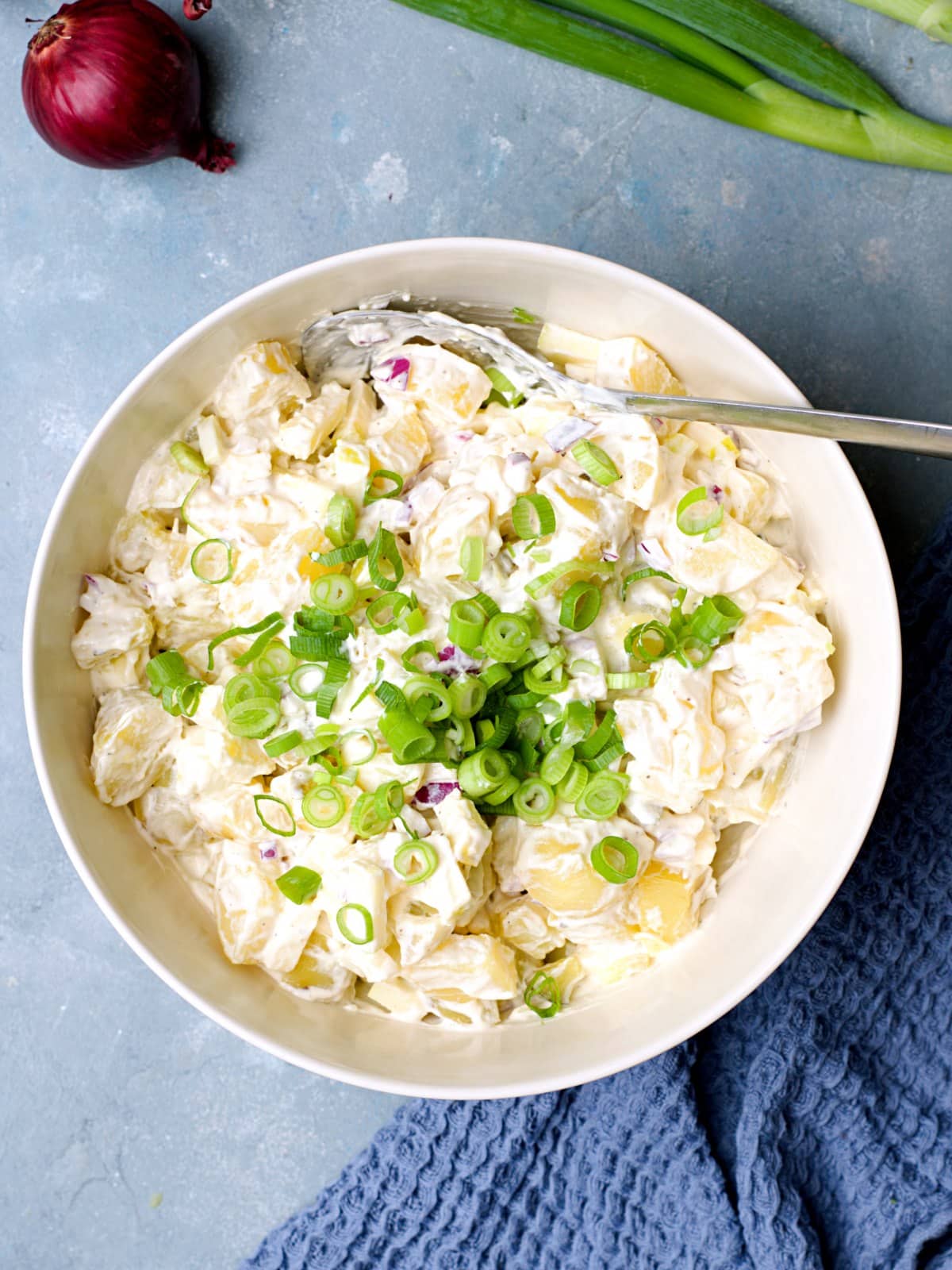 Potato salad in large bowl on blue background with silver ladle. 