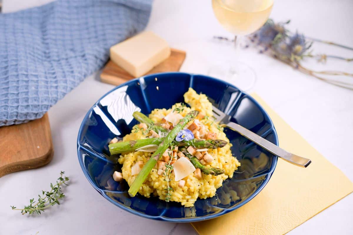 Yellow lemon risotto on blue plate with asparagus and parmesan cheese.