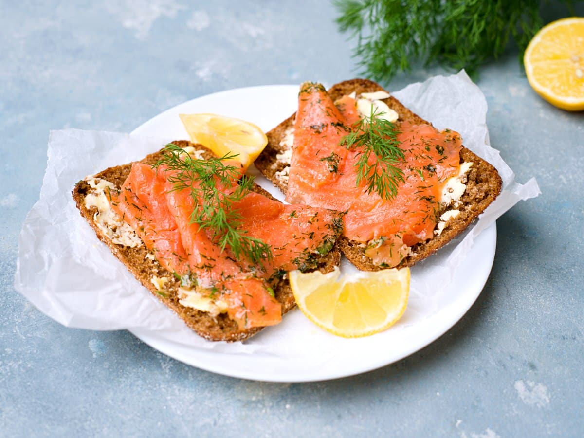 two rye bread slices with gravlax on white plate. 