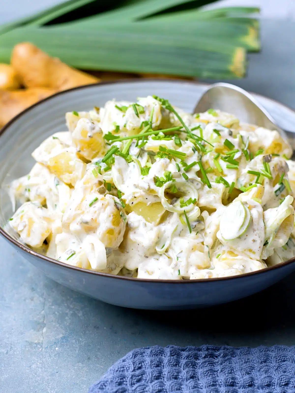 potato salad in blue bowl with potatoes and leek in background.