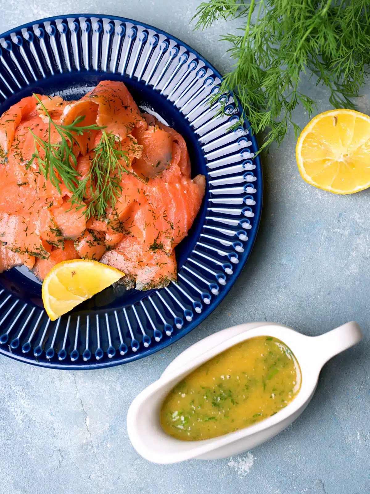 A large plate with cured salmon and lemon wedges with some dill mustard sauce.