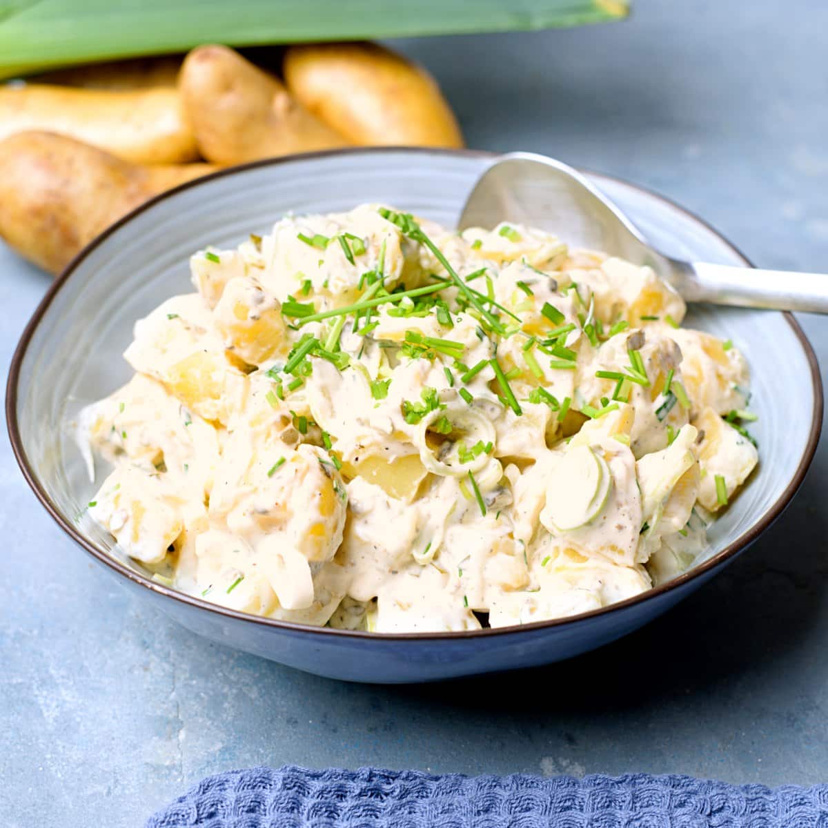 Potato salad with white dressing in blue bowl decorated with chives.